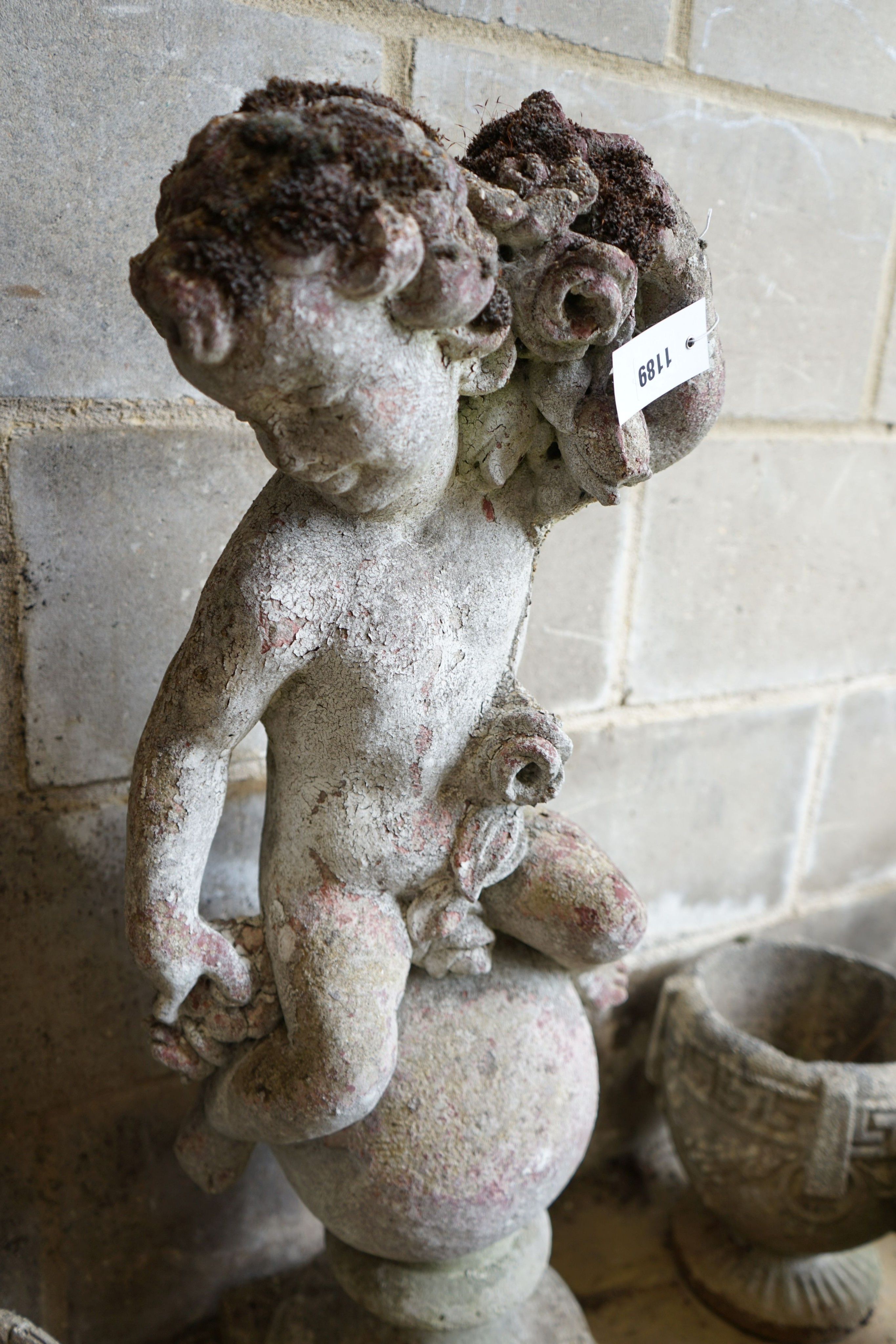A reconstituted stone seated cherub and orb garden ornament, height 84cm